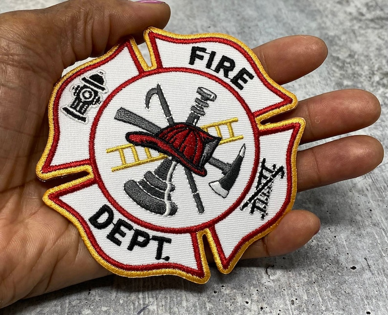 Op de afbeelding: Een witte geborduurde patch met een rood, geel en zwart brandweerlogo. De patch toont een brandweerhelm, een bijl, een ladder en een brandkraan. De tekst "FIRE DEPT." is in zwart op de patch geborduurd.