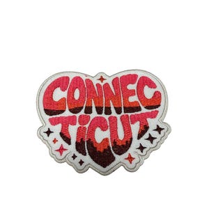 May include: An embroidered patch in the shape of a heart with a white border. The text CONNECTICUT is stitched in a layered, bubbly font using shades of pink, orange, and dark brown. Small four-pointed star accents are scattered around the text.
