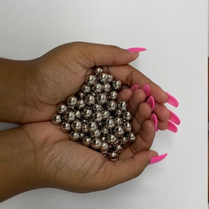 Könnte beinhalten: Eine Hand hält einen Haufen silberner Metallkugeln. Die Kugeln sind glatt und glänzend.