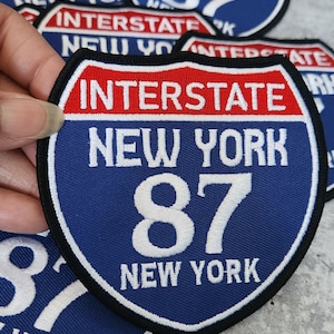 May include: An embroidered patch with the text "Interstate New York 87 New York", in blue and red.