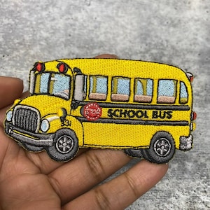 May include: Embroidered patch of a yellow school bus with black wheels and trim. The patch features the words "SCHOOL BUS" in black lettering and a red "STOP" sign. The bus has blue windows and red lights.