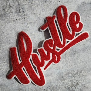 May include: Red felt patch with the word "Hustle" in white outlined letters.