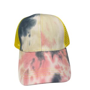 May include: A baseball cap featuring a tie-dye pattern in shades of pink, grey, and cream. The front panels are fabric, while the side and back panels consist of a bright yellow mesh material. The cap includes yellow stitching along the brim.