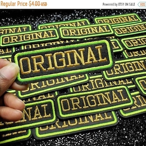 May include: A close-up of a pile of black and green iron-on patches with gold embroidery that reads "ORIGINAL".