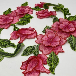 May include: Pink and green embroidered floral applique with a vine design. The applique features several pink flowers with green leaves and stems.