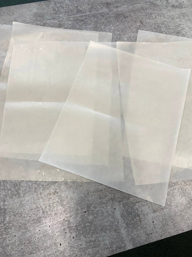 May include: Four sheets of white parchment paper, stacked on top of each other, on a grey textured surface.