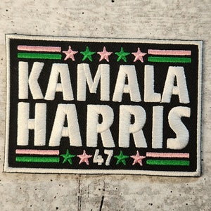 May include: Black and white embroidered patch with the text "KAMALA HARRIS 47" in white. The patch has green and pink stripes and stars.