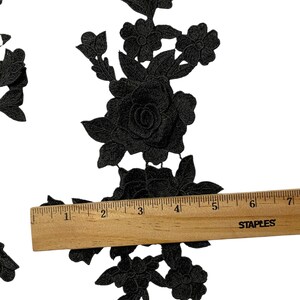May include: Black floral lace applique featuring rose and leaf patterns. A wooden ruler indicates the applique is about 15 cm long. The applique is set against a white backdrop.