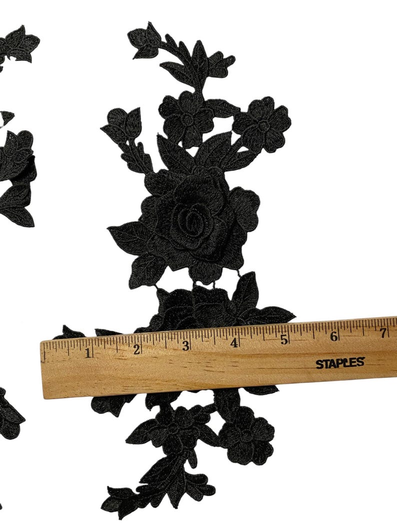 May include: Black floral lace applique featuring rose and leaf patterns. A wooden ruler indicates the applique is about 15 cm long. The applique is set against a white backdrop.