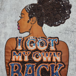 Peut inclure: Un patch en tissu marron avec une silhouette noire et blanche d'une femme avec un chignon. Les cheveux de la femme sont faits de paillettes. Le texte "I GOT MY OWN BACK" est écrit en paillettes orange, blanches et bleues.