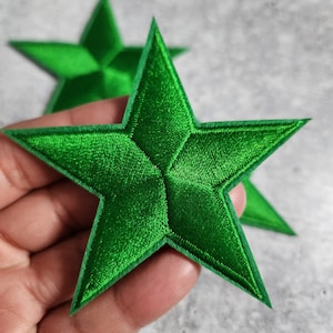 May include: Two green felt star-shaped patches. The stars are five-pointed and have a slightly raised, textured surface.