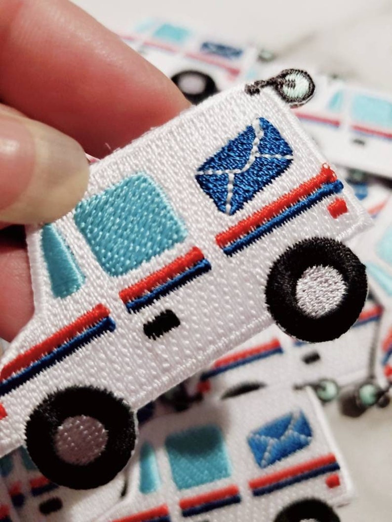 Pu&ograve; includere: Toppa da stirare ricamata bianca di un camion postale con una busta blu, strisce rosse e blu e ruote nere.