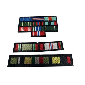 Puede incluir: Tres parches rectangulares bordados con barras de cintas de estilo militar de colores. El parche superior tiene un bloque de siete cintas, mientras que los parches central e inferior son filas horizontales individuales con bordes negros.