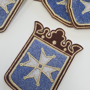 May include: A blue and gold embroidered patch with a white Maltese cross in the center. The patch has a brown felt backing and a gold embroidered border.