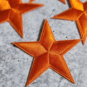 Puede incluir: Cuatro parches de estrellas de fieltro naranja. Las estrellas son de cinco puntas y tienen una textura ligeramente en relieve.