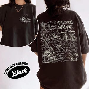 May include: A black t-shirt featuring a small white graphic of a salt shaker and herbs on the front chest. The back displays a large white graphic with the text Practical Magic, a house, a margarita glass, and various witch-themed illustrations.
