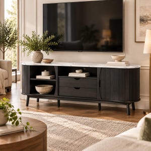 May include: A black media console with a white marble top, featuring two central drawers, open shelving on the left, and two side cabinets with vertical fluted detailing. The unit is supported by four tapered legs and sits below a large flat screen television.