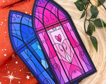 May include: Two arched stickers featuring a stained glass window design. One sticker displays shades of blue, while the other features vibrant pink and purple tones with a central tulip motif. Both have black outlines and intricate scrollwork.