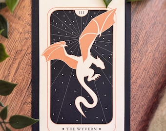 May include: A rectangular tarot-style card featuring a cream-colored wyvern with peach-toned wings against a dark navy background with white stars. The card displays the Roman numeral III at the top and the text THE WYVERN at the bottom.