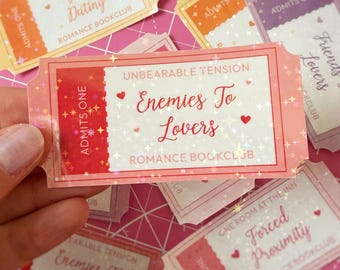 May include: A collection of rectangular stickers shaped like admission tickets, featuring holographic star patterns and various romance book tropes. Text includes "Enemies To Lovers," "Fake Dating," "Friends To Lovers," and "Forced Proximity."
