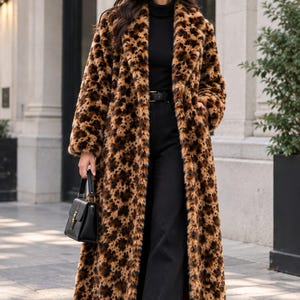 May include: A long, full-length coat featuring a brown and black leopard print pattern. The coat has long sleeves, a wide collar, and a textured, fuzzy finish. It is worn over a black turtleneck sweater, black trousers with a belt, and black shoes.