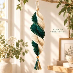 May include: A hanging spiral ornament featuring alternating dark green and cream crochet segments with gold thread accents. The piece includes a wooden bead at the top, a small amber-colored bead at the bottom, and a multi-colored tassel. Text reads: HANDMADE CROCHET DESIGN.
