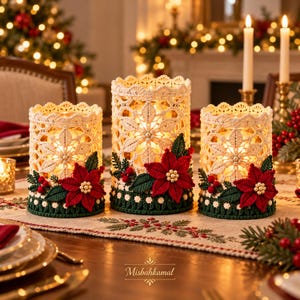 May include: Three cylindrical candle holders wrapped in cream-colored crochet lace with intricate floral patterns. Each holder is decorated with a red crocheted poinsettia, green leaves, and small red berries. The text Misbahkamal is visible.