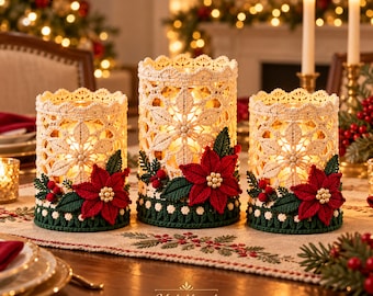 May include: Three cylindrical candle holders wrapped in cream-colored crochet lace with intricate floral patterns. Each holder is decorated with a red crocheted poinsettia, green leaves, and small red berries. The text Misbahkamal is visible.