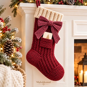 May include: A deep red crocheted Christmas stocking featuring a ribbed texture, a cream-colored cuff, and a large matching red bow. A small pocket on the front holds a card with a gold tree illustration. The text Misbahkamal is printed below.