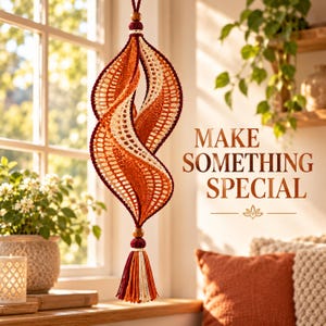 May include: A hanging spiral crochet ornament featuring alternating bands of deep burgundy, burnt orange, and cream yarn. The piece is topped and bottomed with wooden beads and a multi-colored tassel. The text "MAKE SOMETHING SPECIAL" is visible.