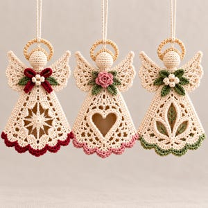 May include: Three hanging crochet angel ornaments in cream yarn, each featuring a halo, wings, and a unique central design. The first has a red bow, the second a pink rose, and the third green leaves. Each dress has a scalloped hem in red, pink, or green.