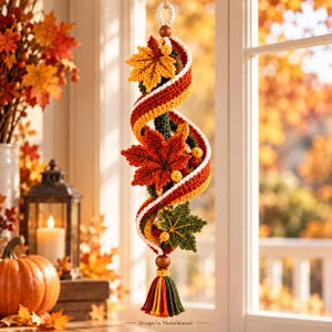 May include: A vertical hanging decoration featuring a spiral crochet design in autumn colors of orange, yellow, red, and dark green. It is adorned with three crocheted maple leaves and small yellow berries, finished with a wooden bead and a tassel.