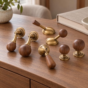 May include: A collection of cabinet hardware featuring a mix of brass and dark wood components. The set includes drop-style pulls with spherical or teardrop wood ends, and stationary knobs with round wood tops on brass bases.