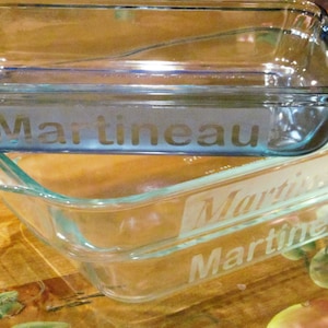 May include: Two clear glass baking dishes stacked on top of each other. The top dish is blue and has the name "Martineau" etched into it. The bottom dish is clear and has the name "Martineau" etched into it twice.
