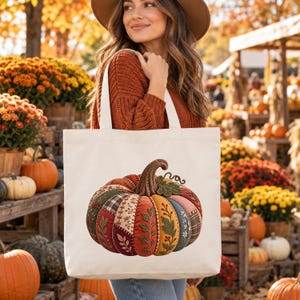 Peut inclure: Un sac fourre-tout en toile blanche orné d'un grand motif de citrouille colorée. La citrouille présente des motifs en patchwork rappelant le tissu, avec des broderies florales, des carreaux et des sections unies dans des tons orange, vert et bleu.