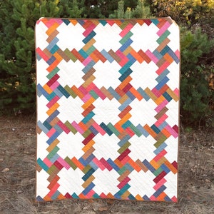 Puede incluir: Una colcha blanca con un patrón geométrico de rayas diagonales de colores. La colcha está hecha con una variedad de telas en tonos de azul, verde, naranja, rosa y rojo.