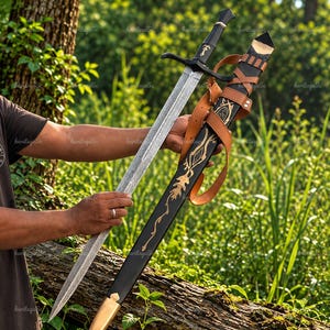 May include: A double-edged steel sword with a black crossguard and pommel, paired with a black scabbard featuring gold-colored leaf-like engravings and a tan leather strap system with metal buckles for carrying the weapon securely.