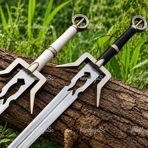 May include: Two metal swords with silver-toned blades and distinct crossguards. One sword features a white handle, while the other has a black handle. Both hilts are topped with a circular pommel design. The blades have a cutout detail.
