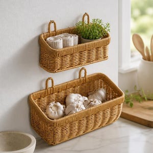 May include: Two rectangular, light brown woven wicker baskets mounted on a wall. The top basket holds two rolled white towels and a small green potted plant. The bottom, larger basket contains several whole white garlic bulbs.