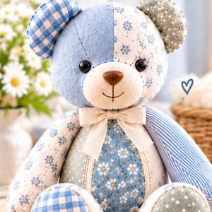 May include: A patchwork teddy bear featuring various blue, white, and sage green fabric patterns including gingham, floral, and polka dots. The bear has black button eyes, a brown nose, and a cream-colored ribbon bow at the neck. Text reads Front View.