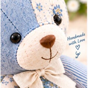 Peut inclure: Un ours en peluche en patchwork compos&eacute; de tissus &agrave; motifs floraux bleus et cr&egrave;me, un museau cr&egrave;me avec un nez et une bouche brod&eacute;s marron, des yeux en boutons noirs et un n&oelig;ud en ruban cr&egrave;me au cou. L'image contient le texte Close-up Detail et Handmade with Love.