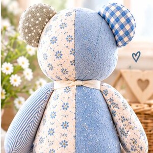 Peut inclure: Un ours en peluche au design patchwork compos&eacute; de divers tissus bleus et cr&egrave;me, incluant des motifs floraux, ray&eacute;s et &agrave; carreaux. L'ours porte un ruban cr&egrave;me nou&eacute; autour du cou et une &eacute;tiquette graphique bleue indiquant Back View.