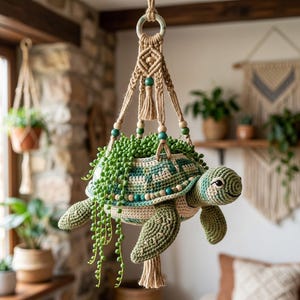 May include: A crocheted turtle-shaped hanging planter featuring a green and cream shell pattern, suspended by a macrame cord with wooden and teal beads. The planter holds a trailing string of pearls plant with long, cascading green stems.