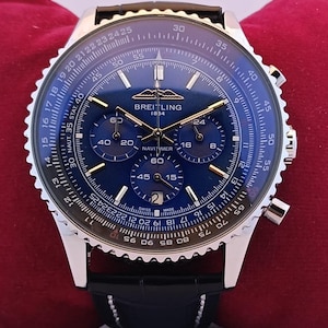 Op de afbeelding: Een Breitling Navitimer 1884 chronograafhorloge met een diepblauwe wijzerplaat, drie sub-wijzerplaten en een datumvenster op de zes-uur-positie. Het horloge heeft een zilverkleurige roestvrijstalen kast, een gekartelde rand en een zwarte lederen band.