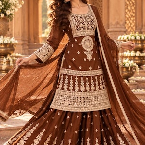May include: A brown three-piece outfit featuring a long-sleeved tunic, a flared skirt, and a sheer dupatta. The tunic and skirt are adorned with intricate gold embroidery in floral and geometric patterns. The logo ClassicLifestyleCo is visible.
