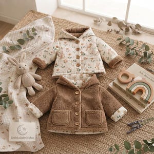 May include: Two reversible hooded jackets with long sleeves and front pockets. One side features a cream fabric with a floral and woodland animal print, while the other side is solid brown textured fleece. Both jackets have four brown buttons.