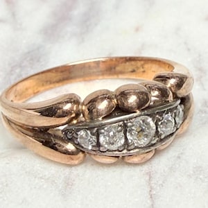 May include: A vintage gold ring with a double band design. The top band features a row of small, round, gold beads. The lower band has a row of five small diamonds set in a silver band. The ring is set on a white surface.