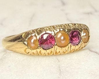 Könnte beinhalten: Ein goldener Ring mit einem strukturierten Band, besetzt mit abwechselnd rosa und pfirsichfarbenen Edelsteinen. Das Design des Rings wird vor einem Marmorhintergrund hervorgehoben. Die Edelsteine haben wahrscheinlich einen Durchmesser von etwa 0,5 cm.