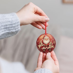 Può includere: Una decorazione natalizia rotonda in ceramica con sfondo rosso e un'illustrazione centrale di Babbo Natale affiancato da due renne. Il design presenta fiocchi di neve dorati e un sottile nastro rosso per appenderlo all'albero.