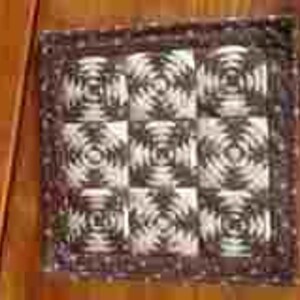 May include: Square quilted trivet with a checkerboard pattern of concentric circles in shades of gray and white. The trivet has a dark brown border and is designed to protect surfaces from hot items.